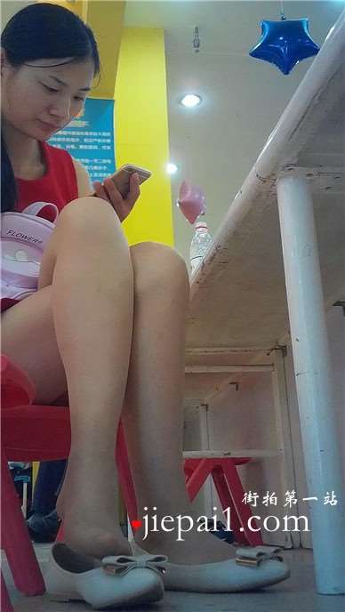 边玩手机边挑些等孩子玩蹦蹦床的红衣少f