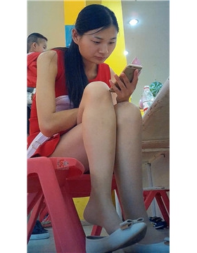 边玩手机边挑些等孩子玩蹦蹦床的红衣少f